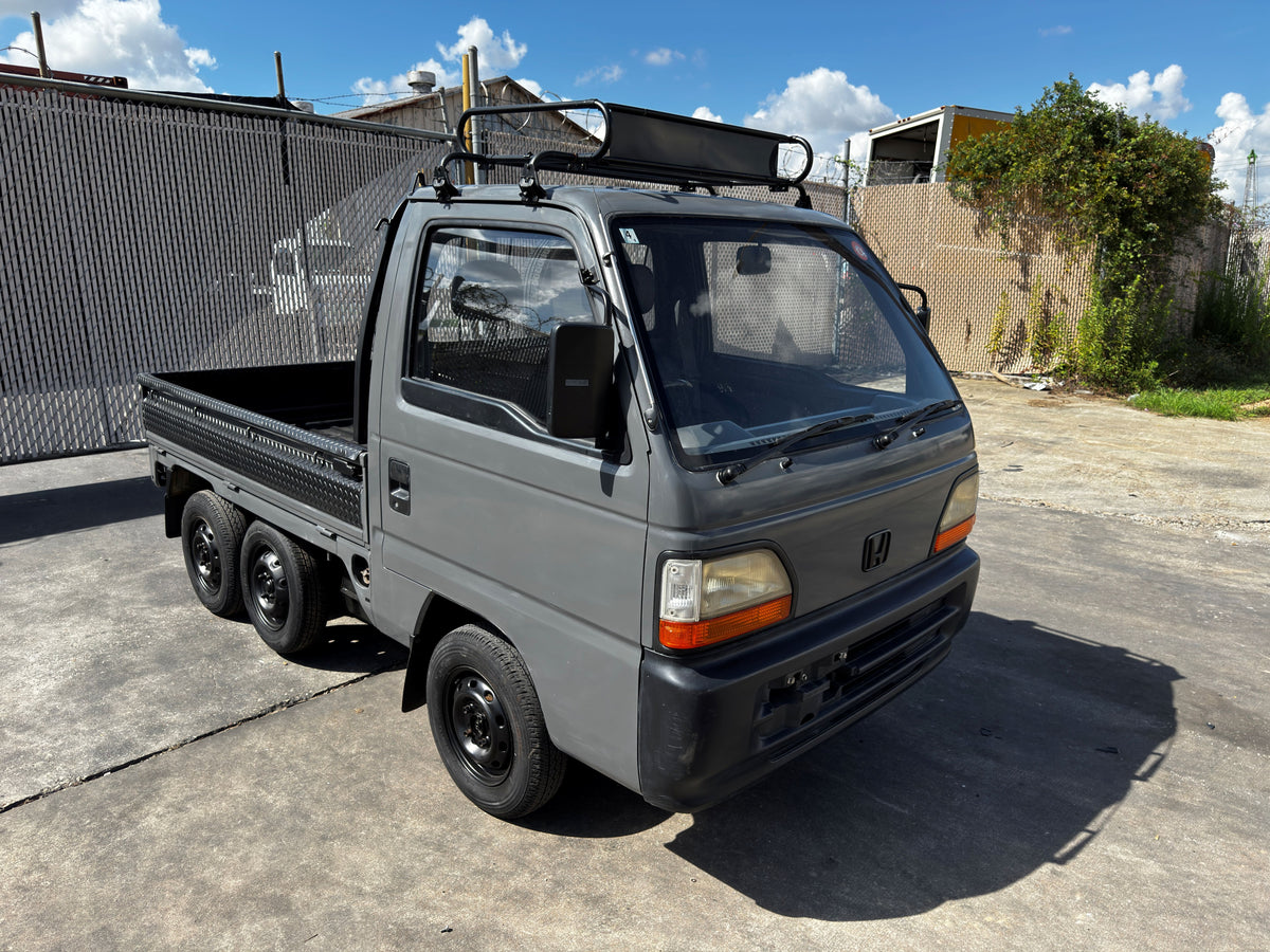 Matte grey Honda Acty kei truck with roof rack and dual rear wheels parked outdoors